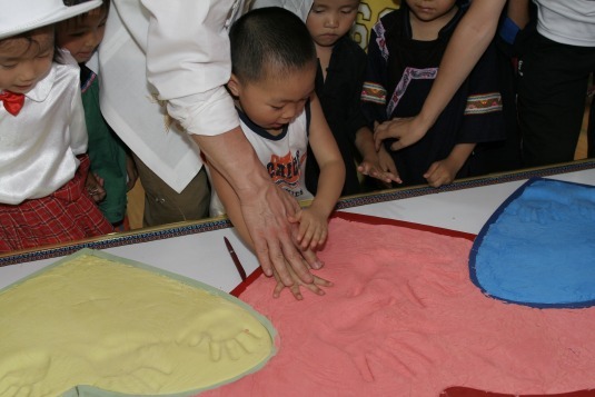 Jackie lends a hand to one of the students as he puts his handprints in the clay.